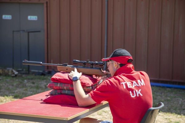A male student in a red Team UK shirt firing a gun from a seated position