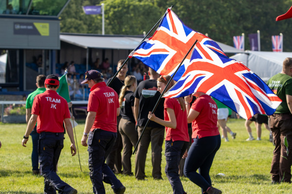 Four students in red Team UK polo shirts, carrying two Union Jack flags 